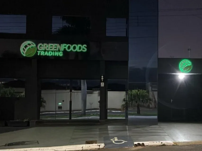 Letreiro verde da Greenfoods Trading aceso na fachada à noite