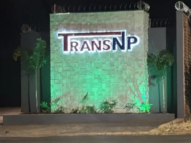 Letras da TransNP com iluminação por trás sobre muro de pedra