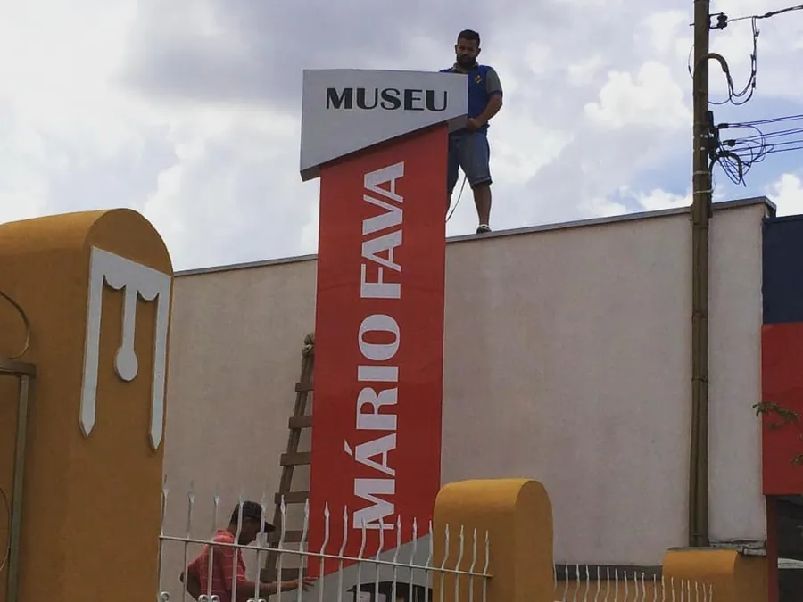Totem vermelho do Museu Mário Fava sendo instalado por um montador